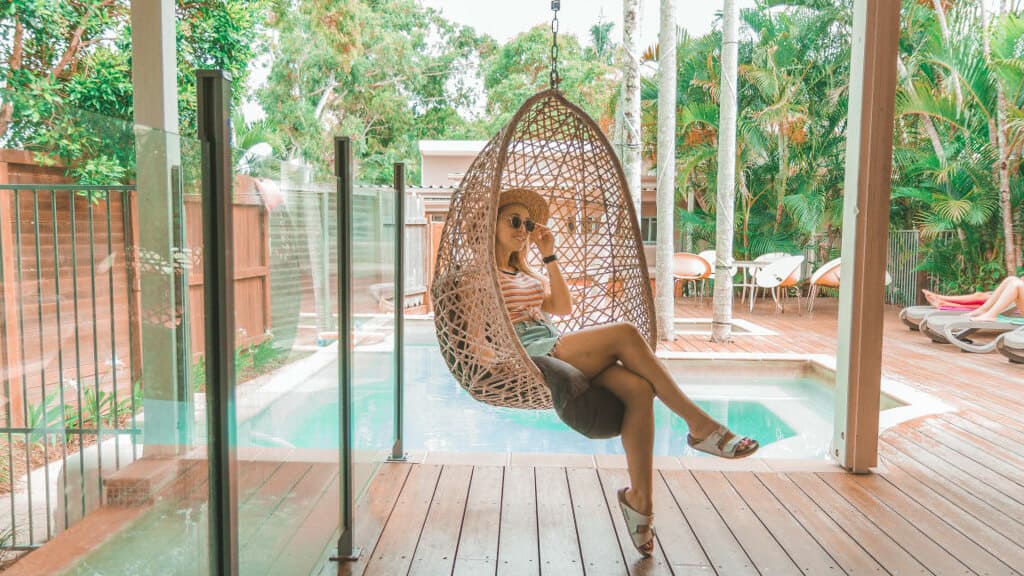 5 Best Hostels in Noosa 7 Girl in hanging chair in front of pool and palms at Noosa Flashpackers hostels in Noosa