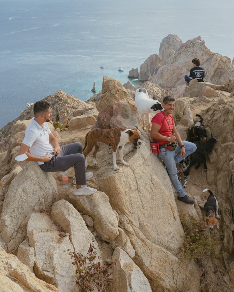 Enrique at the summit of Mt Solmar in Cabo San Lucas with dogs sitting around him on the rocks