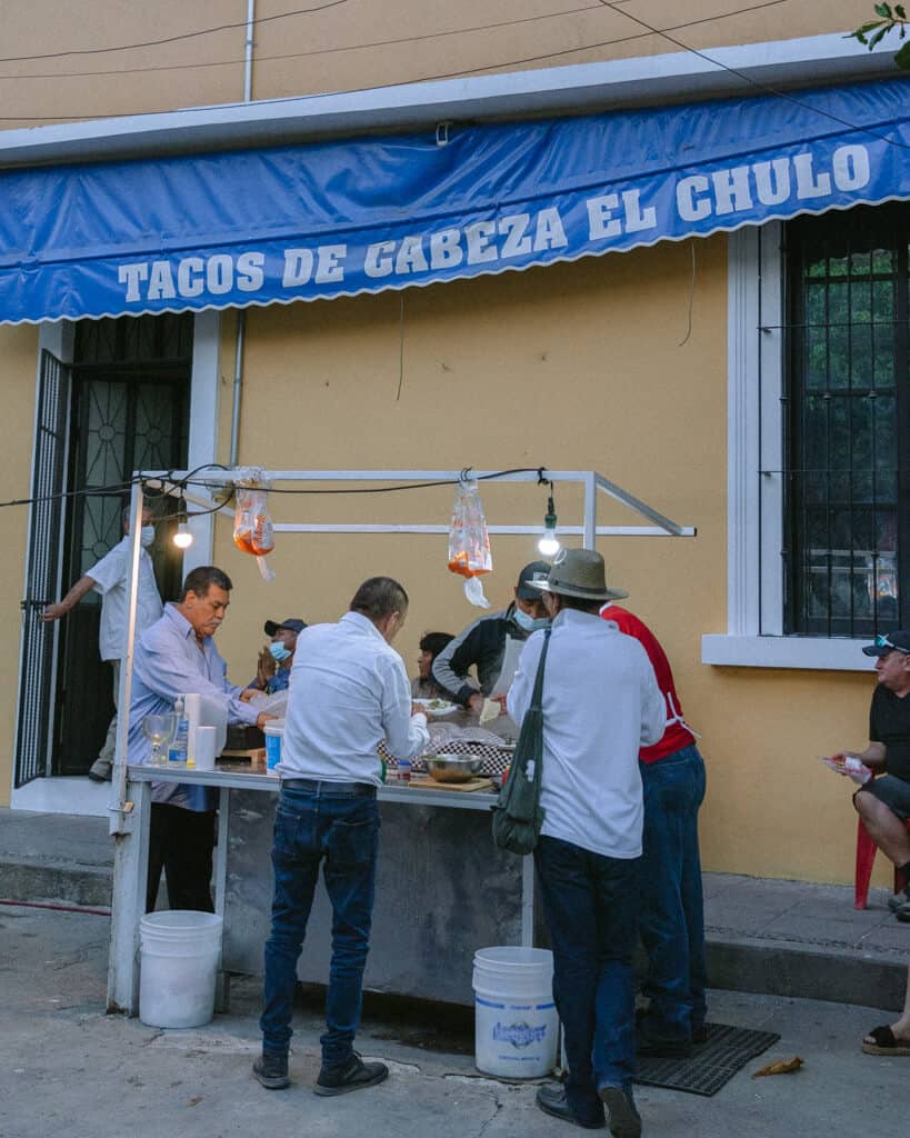 A street side taco stall in Puerto Vallarta with local men crowded around adding toppings to their tacos