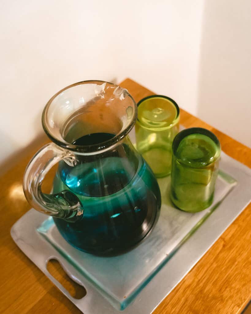 El Patio 77: Sustainable Bed and Breakfast Mexico City 22 A blue tinged glass water pitcher on a silver tray with two green hued glasses