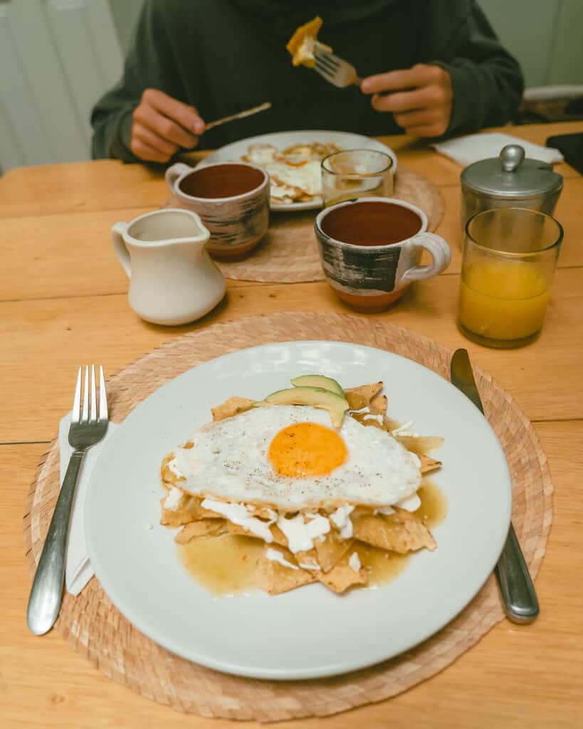 El Patio 77: Sustainable Bed and Breakfast Mexico City 21 A table with breakfast dishes, with a plate of chilaquiles with an egg on top, coffee cups and juice in the background