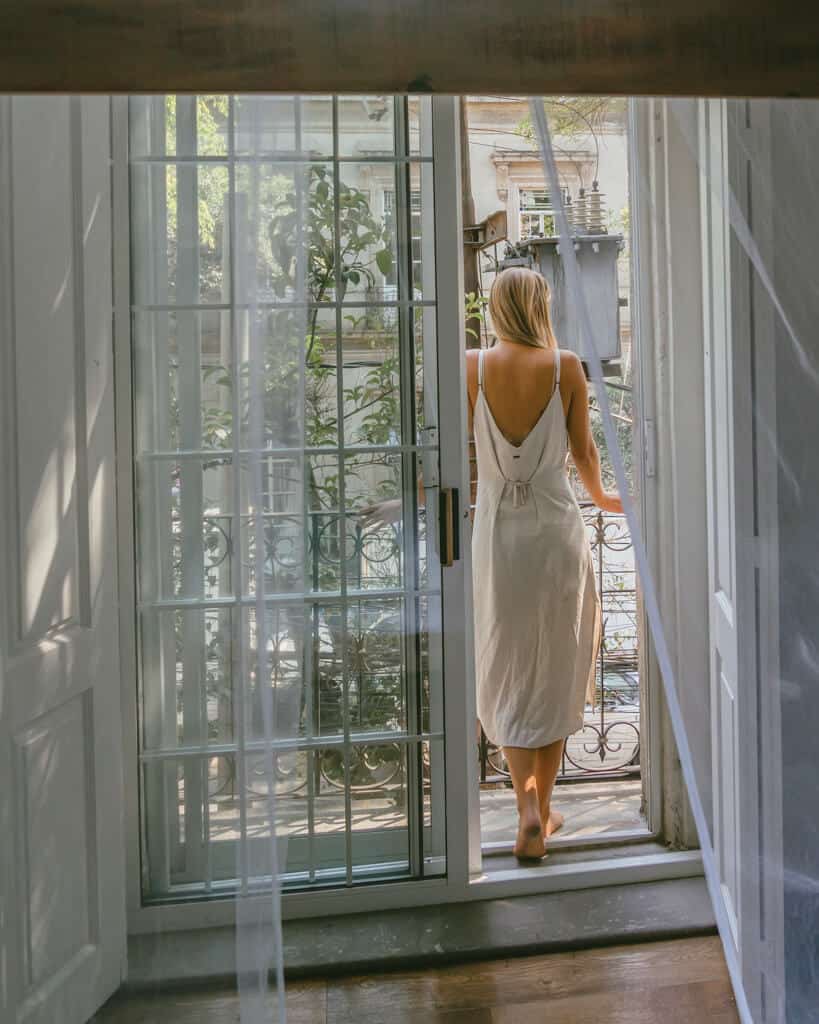 El Patio 77: Sustainable Bed and Breakfast Mexico City 12 Sally standing on a hotel balcony, seen through an open door with ornate balcony railings a sheer curtain over the window