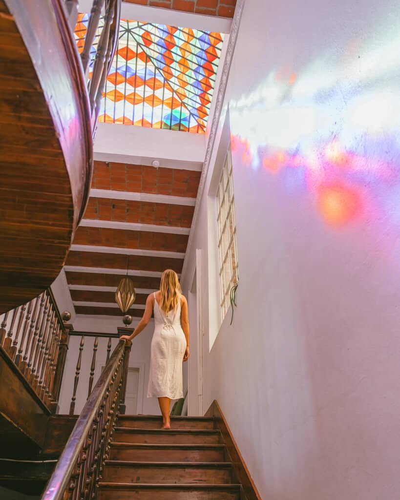 El Patio 77: Sustainable Bed and Breakfast Mexico City 18 Sally walking up a staircase with a colourful stained glass window in the ceiling casting colourful light on the walls