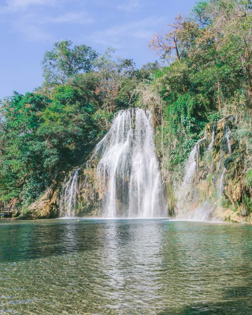 How to Visit Puente de Dios: Tamasopo, Huasteca Potosina 11 Cascadas de Tamasopo in Huasteca Potosina features multiple streams of water cascading down moss-covered rocks into a clear turquoise pool. The lush greenery and bright blue sky frame the serene natural scene.