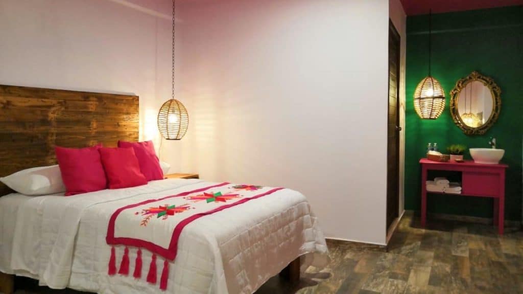 Huasteca Potosina: Guide to Mexico's Waterfall Wonderland 45 A cozy room in Hotel Boutique Santa Lucia Huasteca Potosina with a queen bed dressed in white linens, pink pillows, and an embroidered runner. A green accent wall with a golden mirror and a pink vanity adds colorful charm to the eco-lodge interior.