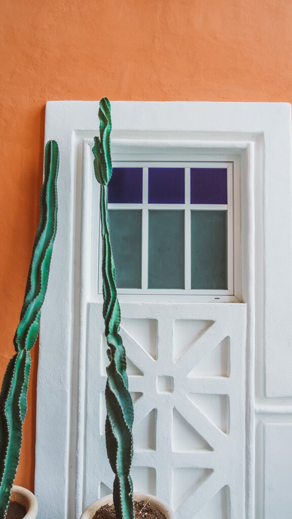 Casa Tortugas Boutique Hotel - Sustainable Accommodation in Cancun 4 A wall with a stained glass window and detailed window pane with two cacti in front