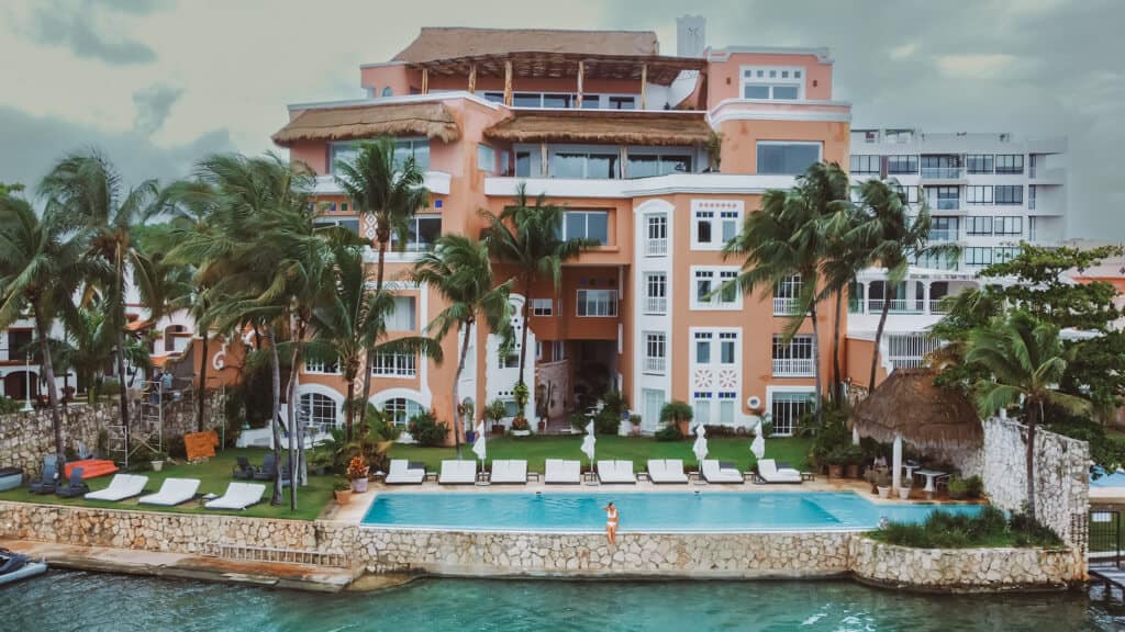 Casa Tortugas Boutique Hotel - Sustainable Accommodation in Cancun 3 A drone shot of a girl sitting on the edge of an infinity pool with a large orange house behind her