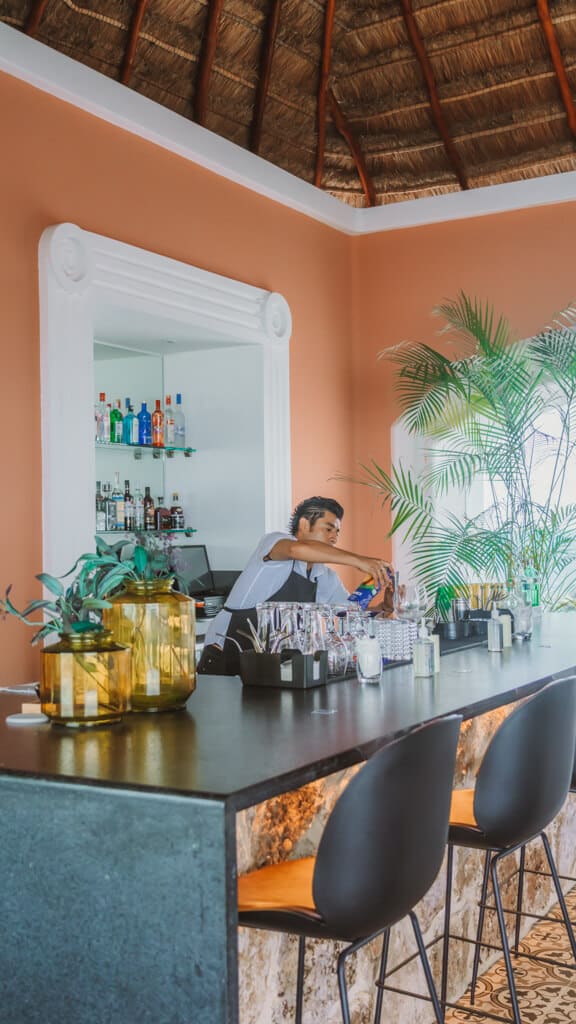 Casa Tortugas Boutique Hotel - Sustainable Accommodation in Cancun 20 A bar tender pouring a drink behind a bar against a bright orange wall
