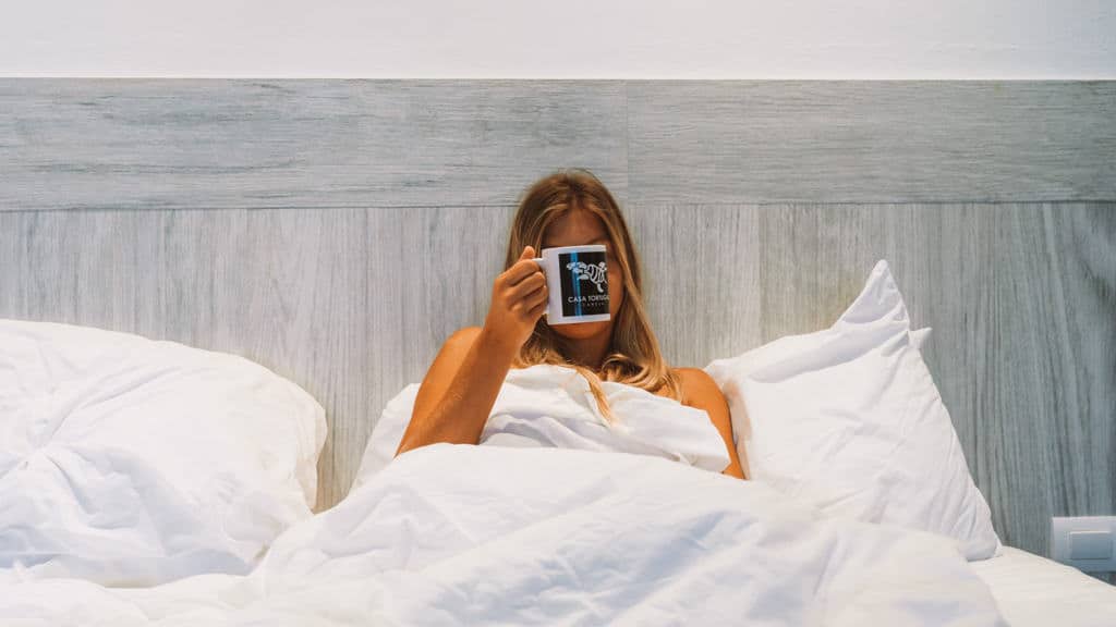 Casa Tortugas Boutique Hotel - Sustainable Accommodation in Cancun 13 Sally sitting in a bed with white bedding holding a coffee cup in front of her face that says Casa Tortugas Boutique Hotel