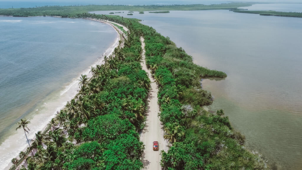 Glamping at Hotel Cielo y Selva in the Sian Ka'an Biosphere Reserve 6 A drone shot of a car driving down a palm lined road with the ocean on one side and a lagoon on the other