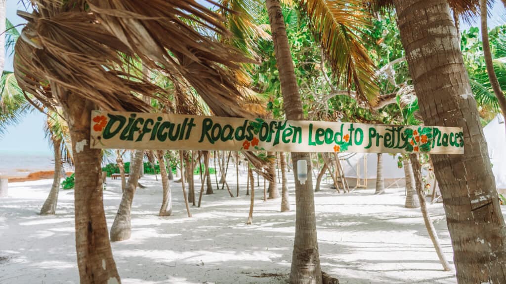 Glamping at Hotel Cielo y Selva in the Sian Ka'an Biosphere Reserve 5 A wooden painted sign in palm trees that says 'difficult roads often lead to pretty places'