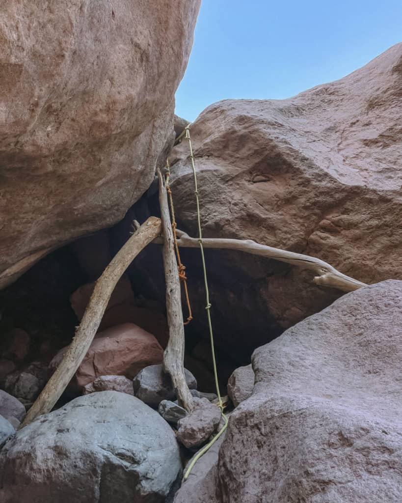Tabor Canyon, Loreto Hiking Guide 9 A makeshift wooden ladder secured with a thick rope ascends through large boulders in a narrow canyon passage, offering a rugged climbing route between the rocks.