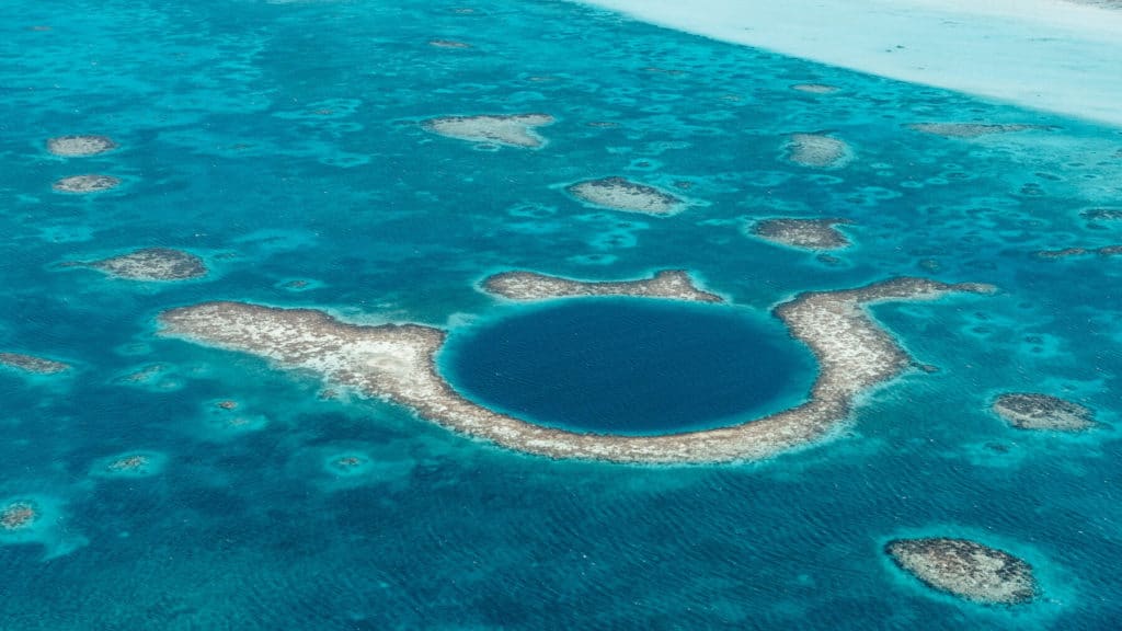 10 Top Things to do in Belize: Your Belize Bucket List 3 Aerial view of the Great Blue Hole off the coast of Belize, showing the deep circular sinkhole surrounded by shallow coral reefs and vivid turquoise waters
