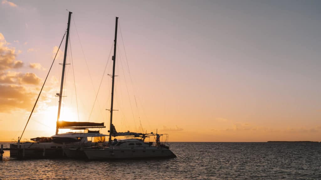 10 Top Things to do in Belize: Your Belize Bucket List 7 A catamaran from Ragga Sailing Adventures docked at sunset in Caye Caulker, Belize, with a soft pastel sky and calm waters creating a peaceful tropical scene.