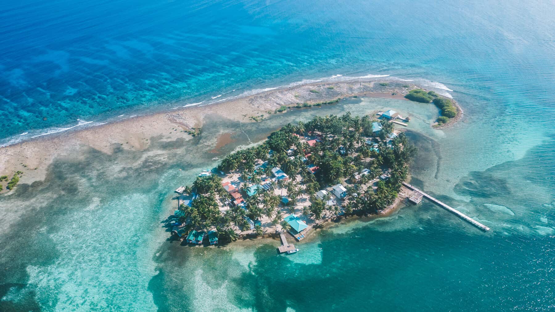 10 Top Things to do in Belize: Your Belize Bucket List 8 A stunning aerial view of Tobacco Caye, Belize, a small palm-covered island surrounded by shallow turquoise waters and a protective reef, with a dock extending into the sea.