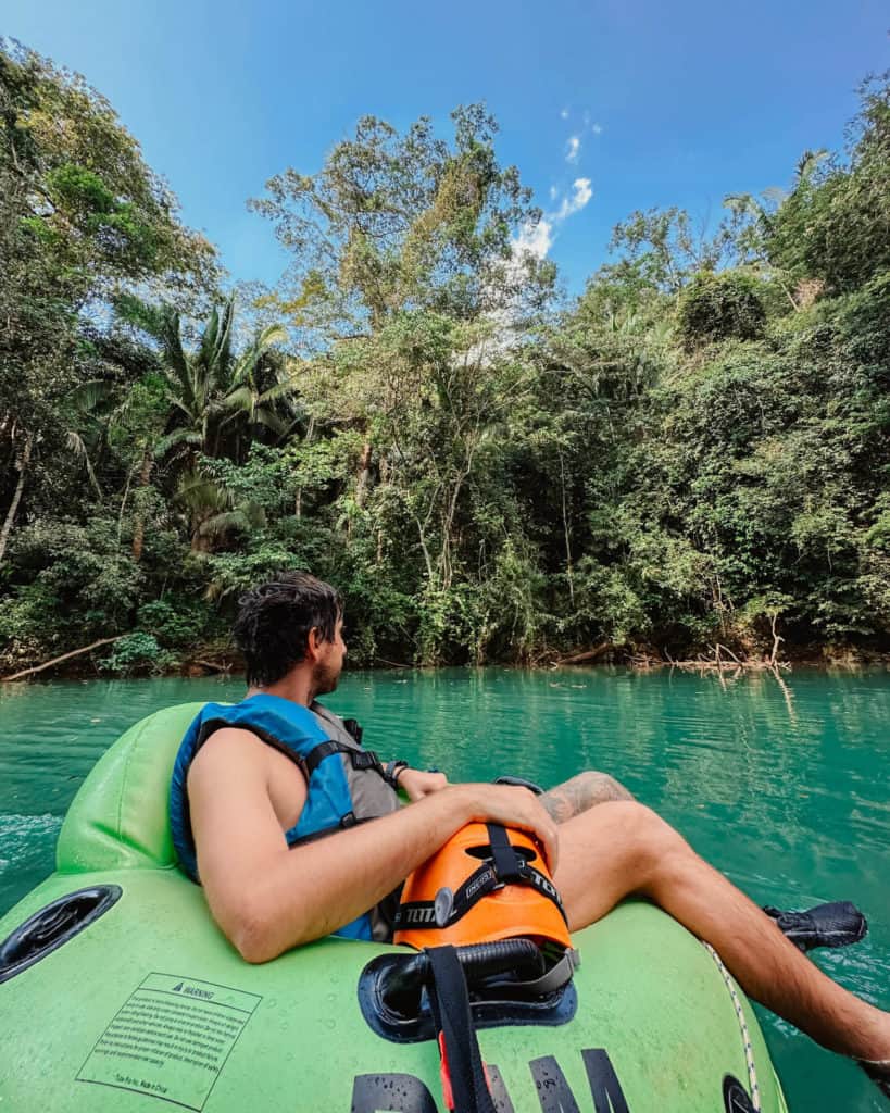 10 Top Things to do in Belize: Your Belize Bucket List 10 Brayden relaxes on a green inner tube as he floats along a turquoise jungle river near San Ignacio, Belize, surrounded by dense tropical foliage under a clear blue sky.