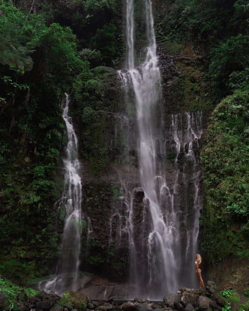 Bajos del Toro Travel Guide: Costa Rica's Waterfall Wonderland 11 Sally standing on a rock with a huge waterfall behind her, with a curtain of water following over sheer black rock in Bajos del Toro
