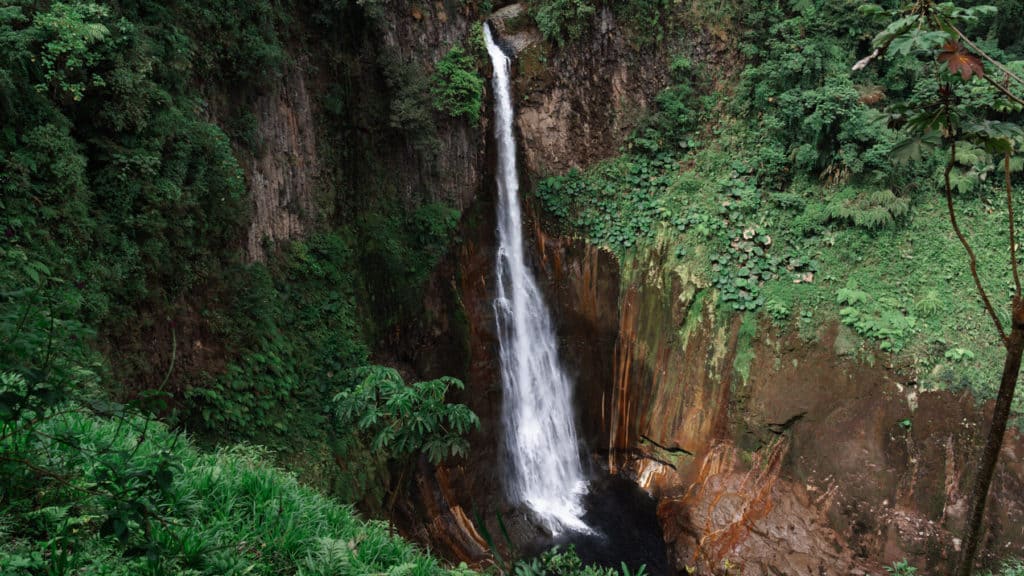 Bajos del Toro Travel Guide: Costa Rica's Waterfall Wonderland 9 An aerial view of a very tall waterfall dropping into a canyon with red coloured rock and greenery in Bajos del Toro
