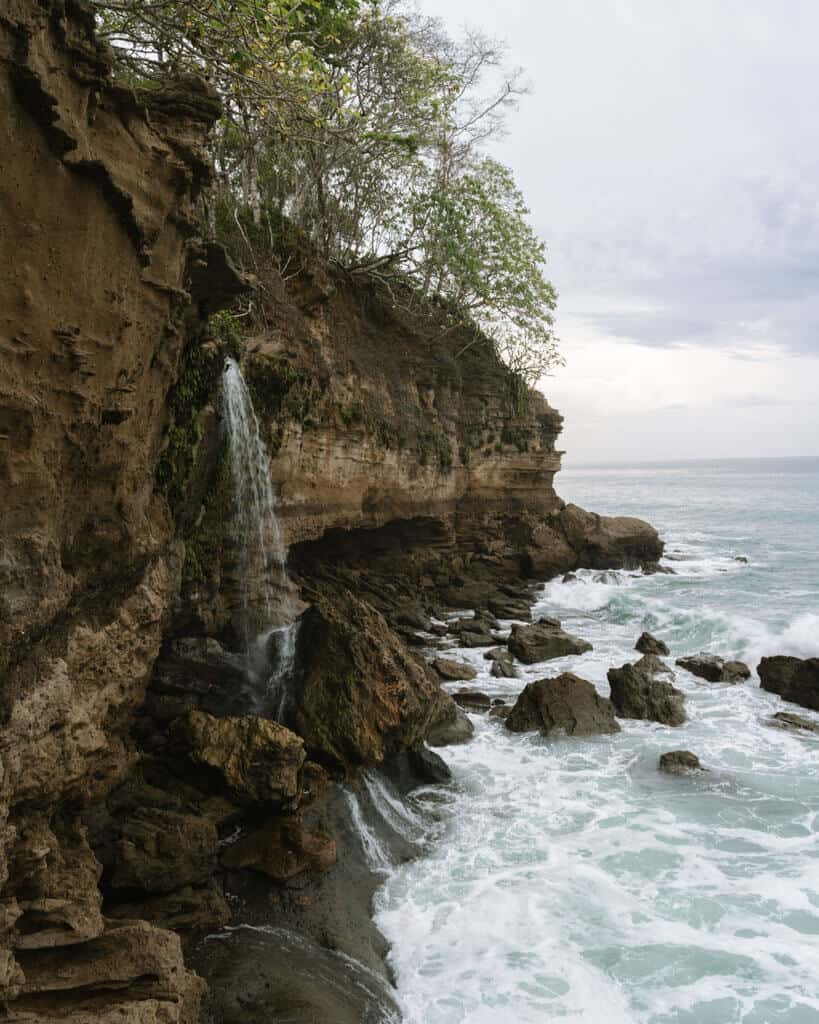A side angle of the El Chorro Waterfall dropping down a steep cliff into the ocean at Playa Cocalito