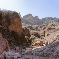 Sally Sees walking in a red rock desert landscape across large boulders in a canyon