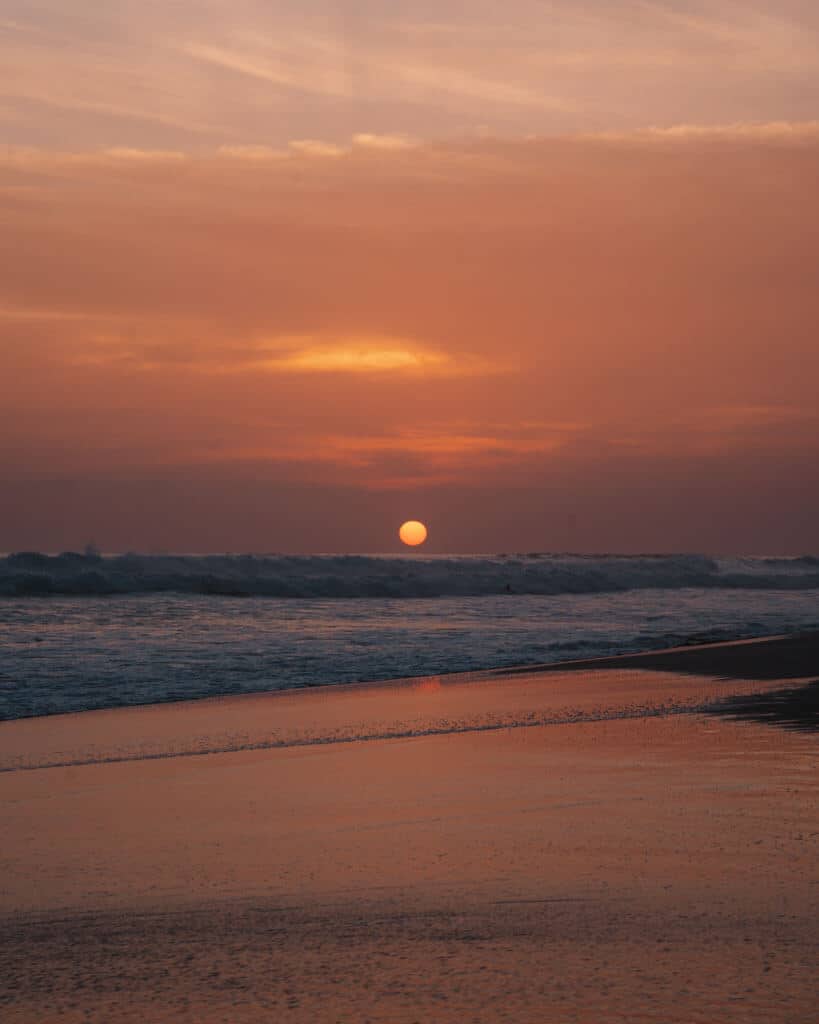 15 Best Things to Do in Montezuma Costa Rica 26 A pink purple and orange hued sunset from the beach, with a flaming orange ball dropping towards the horizon at Santa Teresa