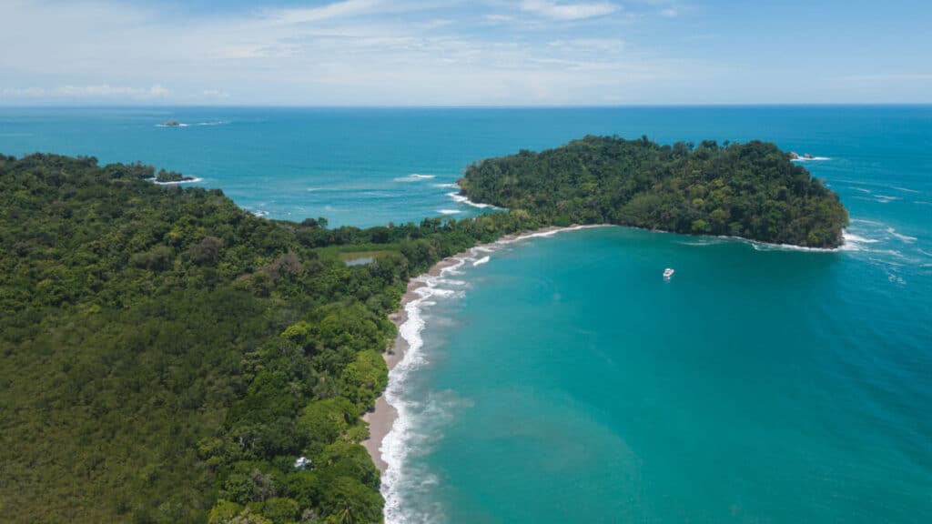 A breathtaking aerial view of the famous Manuel Antonio National Park with its lush green peninsula surrounded by turquoise waters and white sandy beaches.