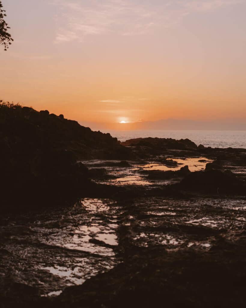 Sunrise at Montezuma beach paints the sky in shades of orange and purple, with rocky tide pools reflecting the sunlight.