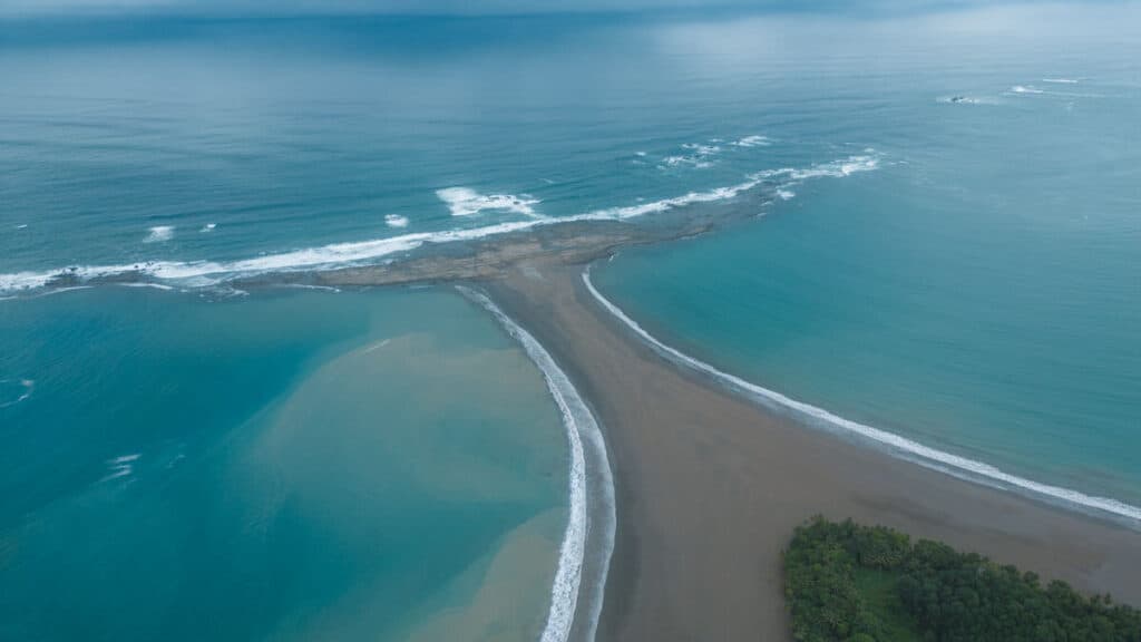 A panoramic aerial view from above of the distinctive whale's tail sandbar at Marino Ballena National Park in Uvita, surrounded by the azure Pacific.