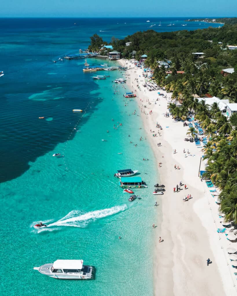 Aerial view of West Bay Beach in Roatan, displaying the vibrant beach life with people and boats on the sparkling turquoise waters.