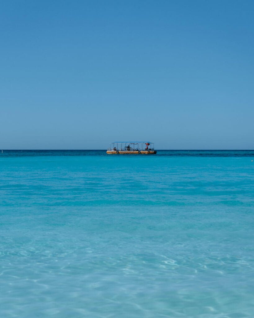 18 Things to Do in Roatan (+ Unethical Things NOT to Do) 13 A yellow boat in the distance on the horizon floating in the aquamarine waters of West Bay Beach