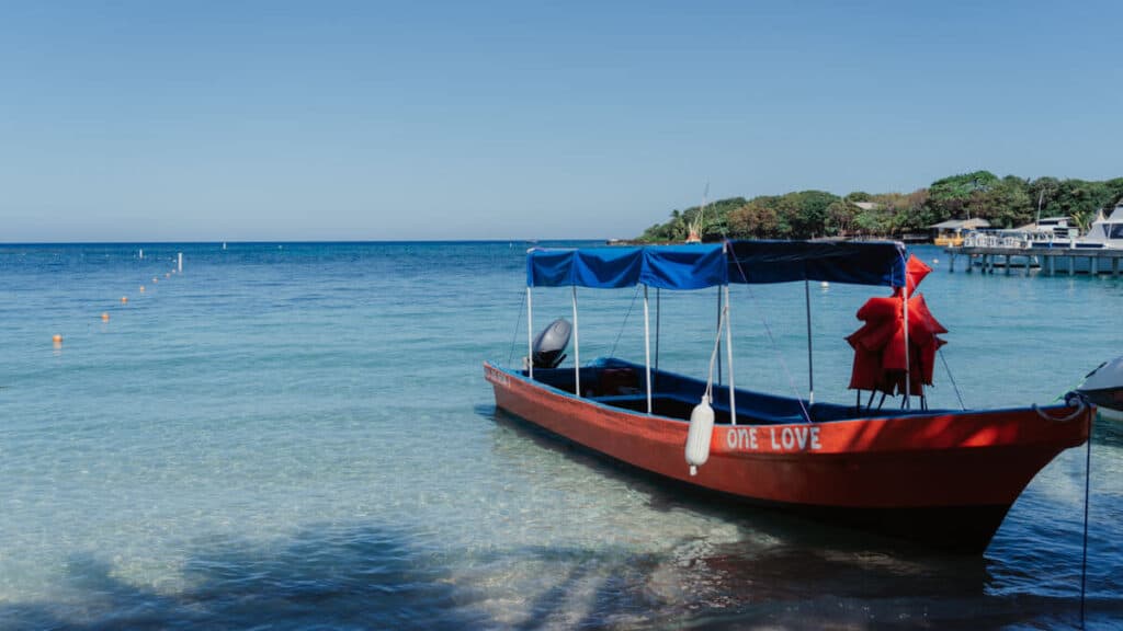 The 'ONE LOVE' boat moored in the serene waters of Half Moon Bay, Roatan, under a clear blue sky.