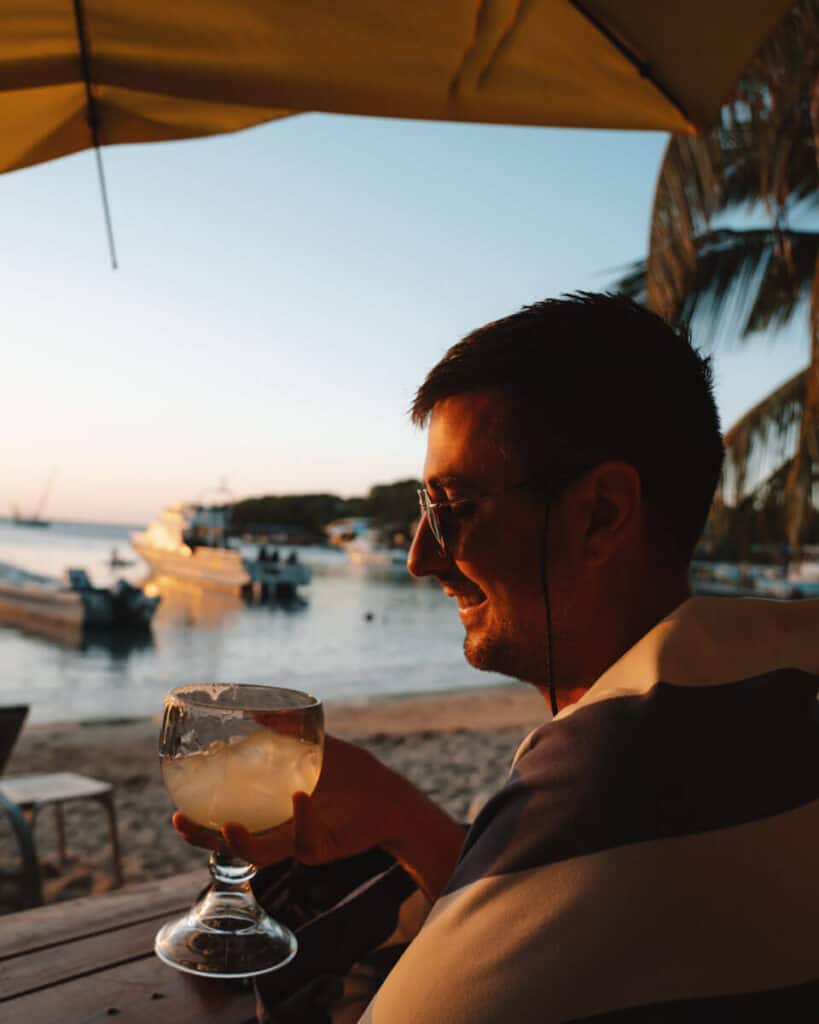18 Things to Do in Roatan (+ Unethical Things NOT to Do) 41 Brayden smiling at his drink, a glass challis style cocktail at Sundowners in West End