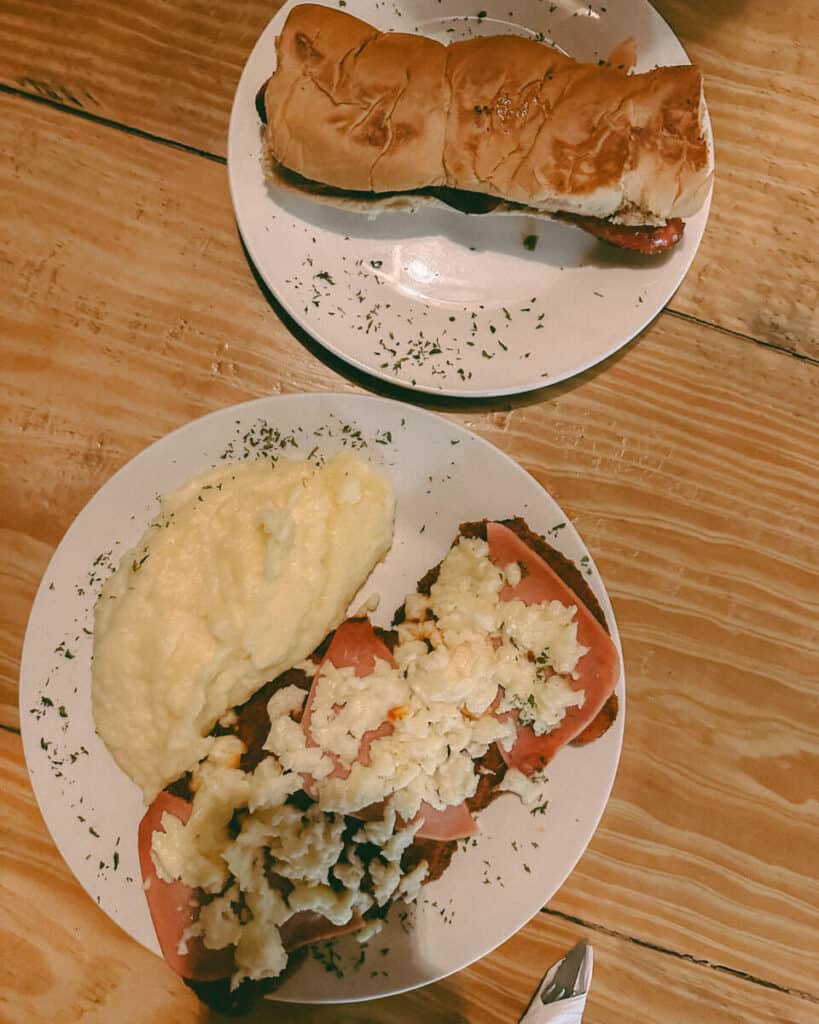 Our Top 10 Restaurants in Utila, Honduras 12 A hearty meal served at Che Pancho, a Utila restaurant, featuring a stuffed sandwich on a plate and a second plate with creamy mashed potatoes and milanesa topped with ham, tomato and cheese