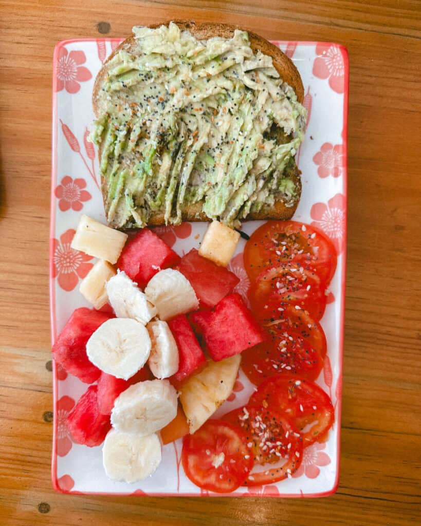 Our Top 10 Restaurants in Utila, Honduras 7 A healthy and colorful meal at a Utila restaurant, with avocado toast sprinkled with seeds, a side of fresh banana, watermelon, and tomato slices on a floral plate at Josie's Cafe
