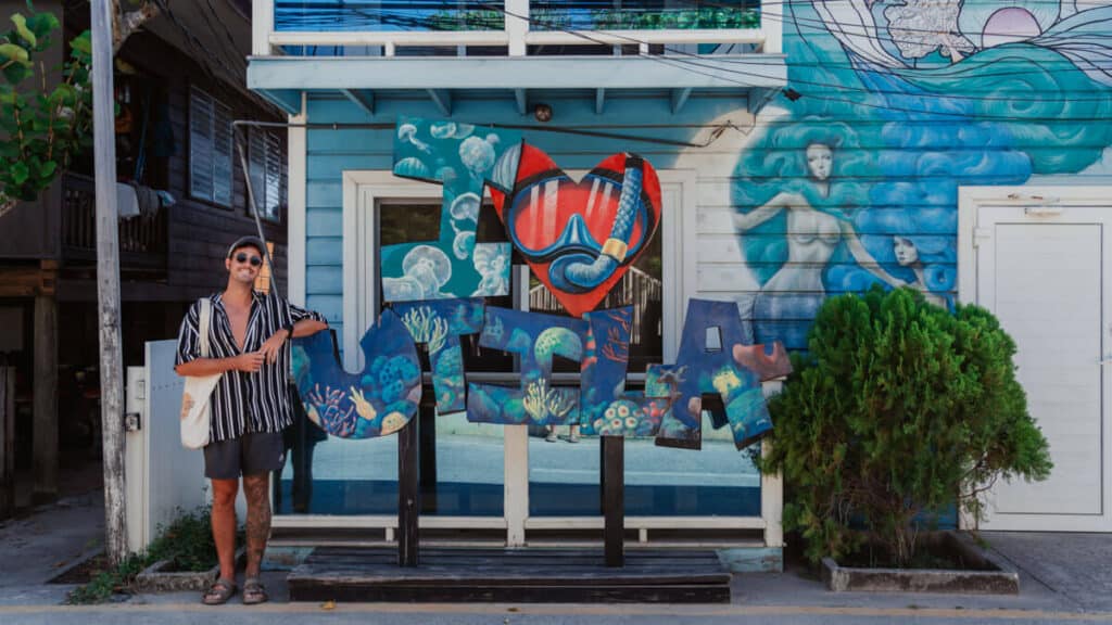 Brayden stands in front of an I ❤️ Utila vibrant mural featuring marine life and a large snorkel mask in Utila Honduras