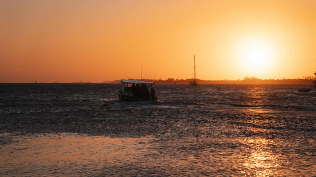 16 Best Things to Do in Utila, Honduras (Diving & More) 40 A boat filled with passengers makes its way across shimmering golden waters under the setting sun, creating a serene end-of-day scene on an Underwater Vision night dive