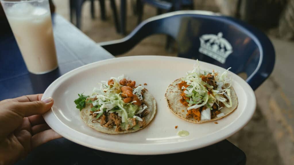 San Pancho Mexico Travel Guide: Tropical Bliss in Nayarit 33 A hand holding out an oval shaped plastic plate with two tacos on it, topped with lettuce, beans and salsa
