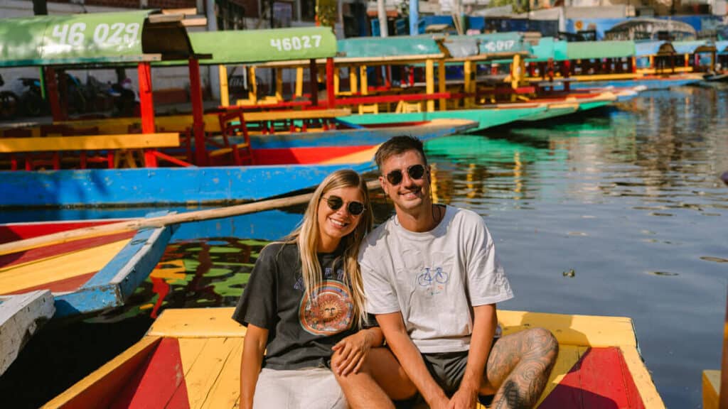 A landscape shot of Sally and Brayden sitting close together on a colorful trajinera in the Canals of Xochimilco.