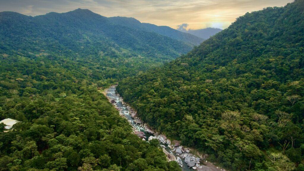 The Perfect 2 - 3 Week Honduras Itinerary 21 A landscape scene of Rio Cangrejal, filled with huge boulders on a blue sunny day with some fluffy clouds in the sky, and mountains and greenery around the river