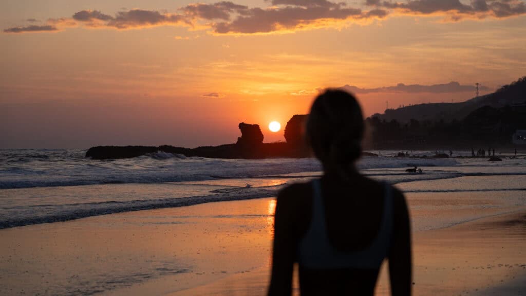 Ultimate 2 Week El Salvador Itinerary 5 Stunning silhouette of Sally against a vibrant sunset in El Tunco, El Salvador, with the sun descending between iconic rock formations at the beach.