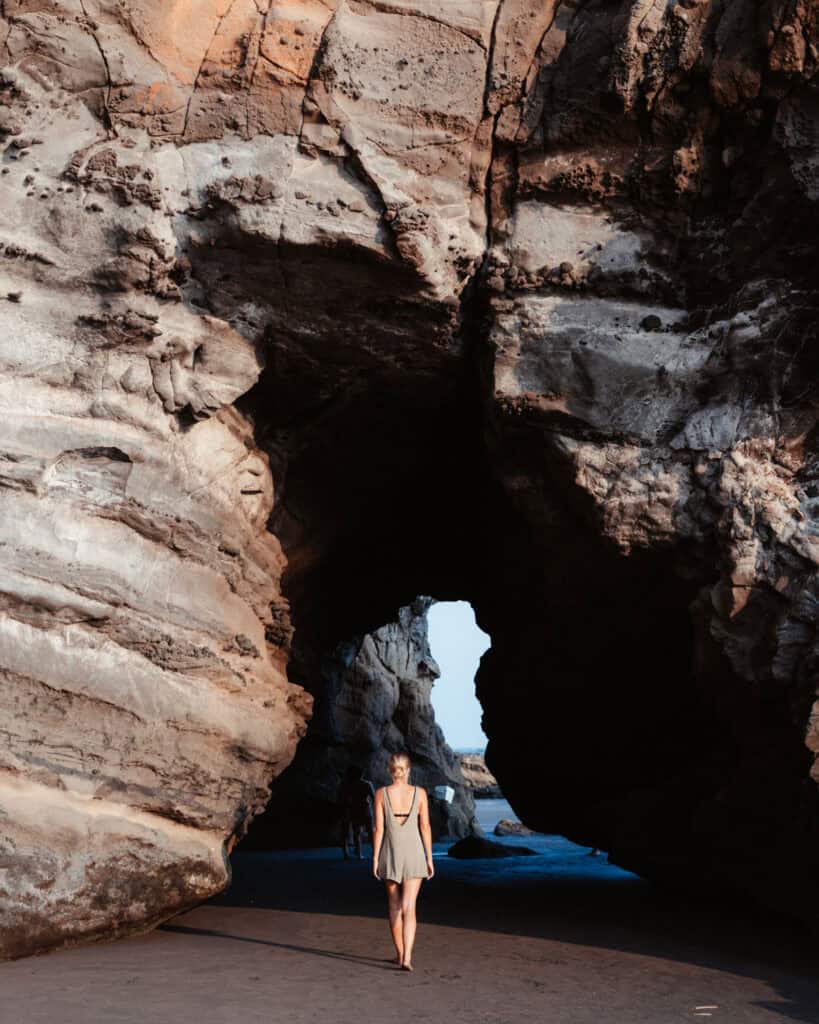 20 Best Things to Do in El Tunco & Surrounds, El Salvador 37 Sally exploring a sea cave in El Zonte, with sunlight streaming through the cave opening, highlighting the rugged textures of the cave walls and the serene beach outside.