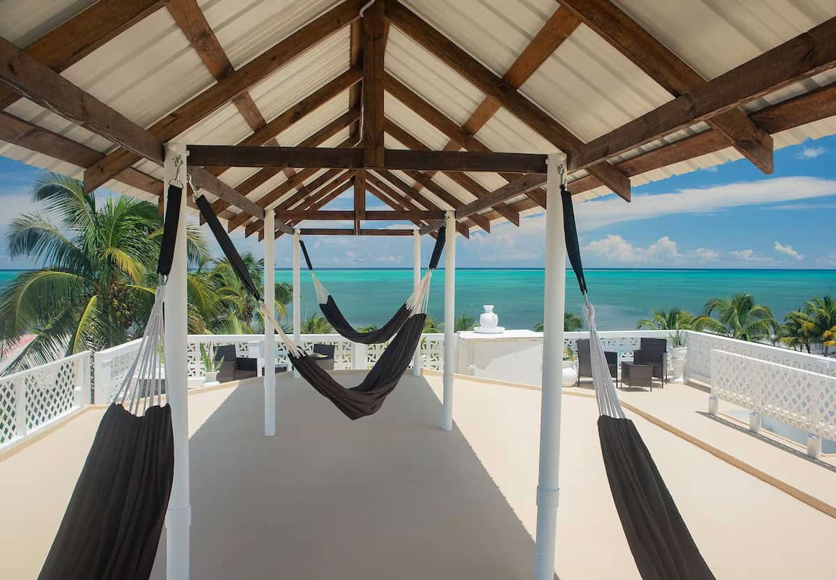 Where to Stay in Caye Caulker: 16 Options For All Budgets 16 A shaded rooftop terrace in Treetrops Hotel Caye Caulker features multiple hammocks under a wooden-beamed roof, with panoramic views of the turquoise Caribbean Sea and palm trees in the distance.