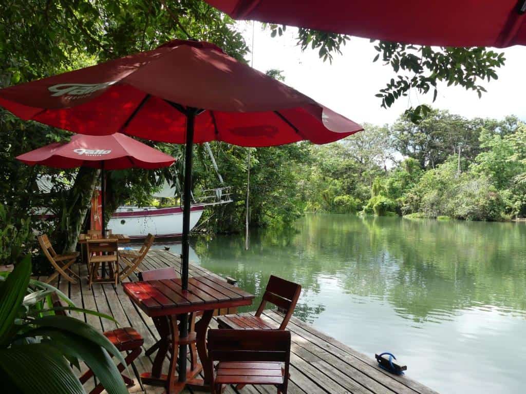 Complete Guide to Rio Dulce Guatemala 12 Riverside wooden deck with outdoor seating and red umbrellas at Hotel Kangaroo in RĂo Dulce, Guatemala, surrounded by lush tropical jungle.