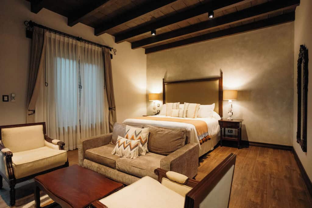 Where to Stay in Antigua Guatemala: Best Boutique Stays 27 A luxurious bedroom at Los Pasos hotel in Antigua Guatemala, with gold features and tones with a nice bed styled with cushions and blankets and a window letting in golden light.