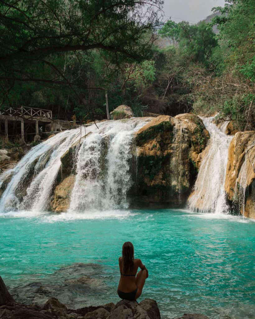 Cascadas El Chiflon: Without a Tour + Overnight Stay 31 Sally is sitting alone on a rock near the pool of Cascada El Suspiro, gazing at the powerful waterfall. The scene is surrounded by lush greenery, enhancing the tranquil atmosphere.