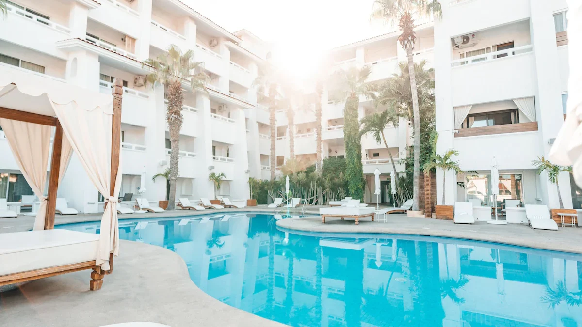 A pool scene at the Bahia Hotel & Beach House in Cabo San Lucas with white pool lounges and palm trees. 