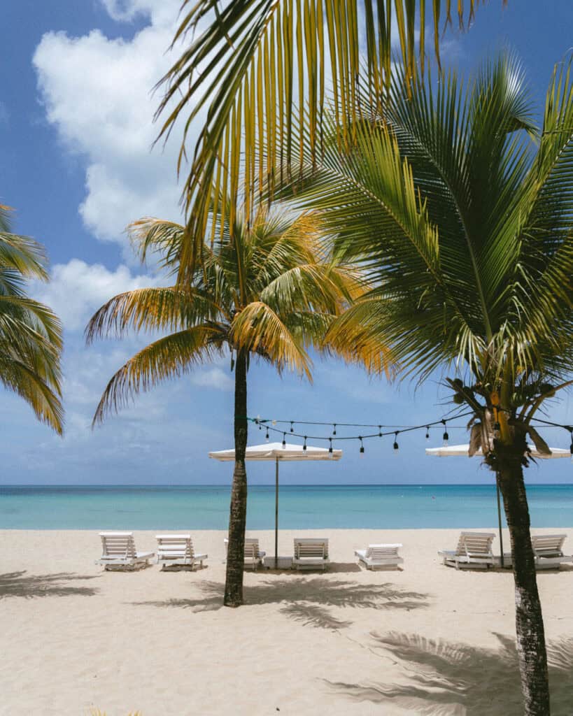 Nicaragua Travel Guide: Land of Lakes and Volcanoes 25 Rows of white lounge chairs and umbrellas spread across the sandy beach of Arenas Beach Club on Big Corn Island, with palm fronds framing the view of the sparkling sea.