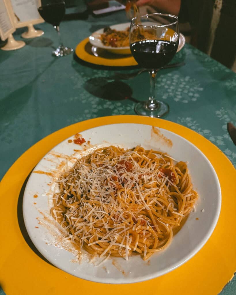 Big Corn Island, Nicaragua: The Underrated Corn Island 44 A plate of spaghetti topped with grated cheese and tomato sauce, paired with a glass of red wine, set on a green tablecloth at La Princesa de la Isla on Big Corn Island.
