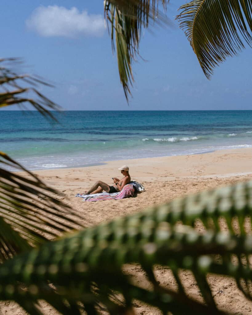Big Corn Island, Nicaragua: The Underrated Corn Island 7 Brayden relaxing on a towel at Long Bay Beach reading his ereader, framed by the swaying fronds of a nearby palm tree.