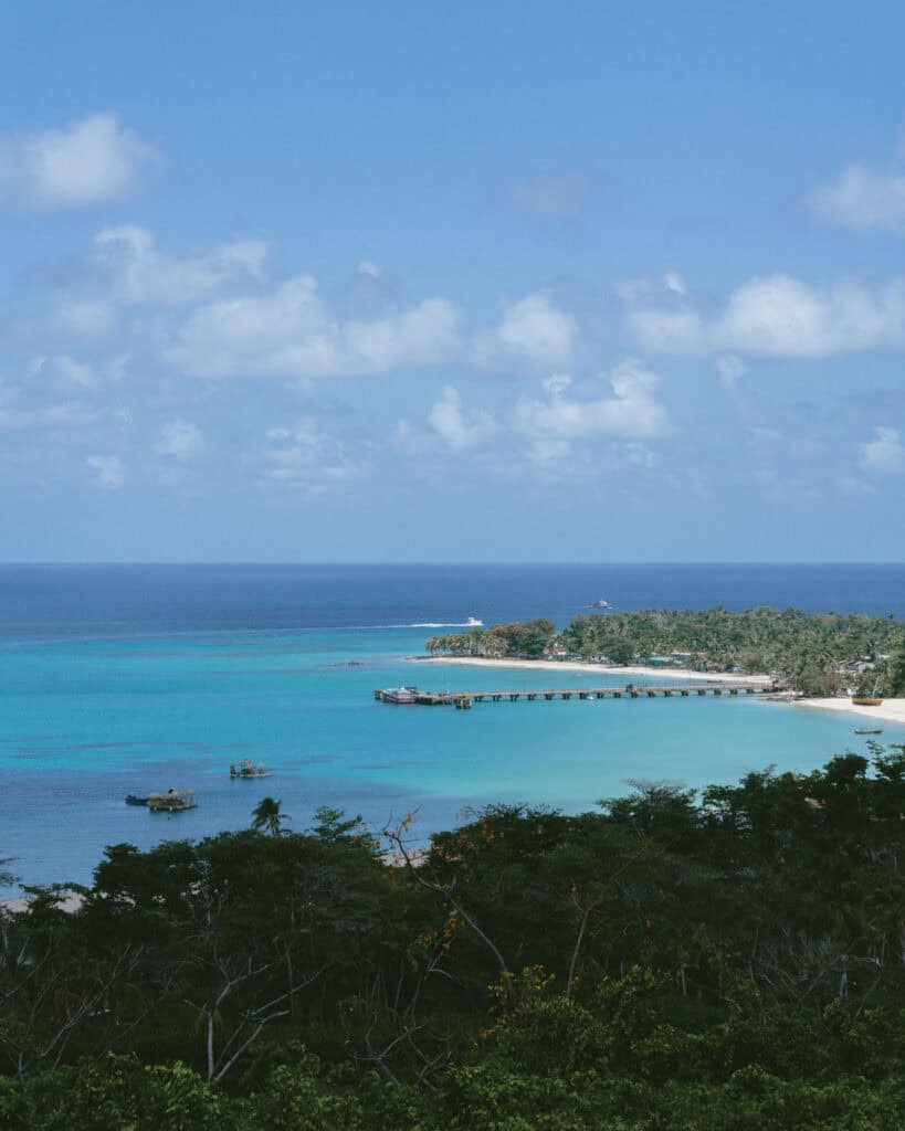 Big Corn Island, Nicaragua: The Underrated Corn Island 1 A panoramic view from Quinn Hill Mirador, highlighting the expansive ocean with varying shades of blue and a coastline dotted with palm trees. You can clearly see a long dock in bright, turquoise waters.